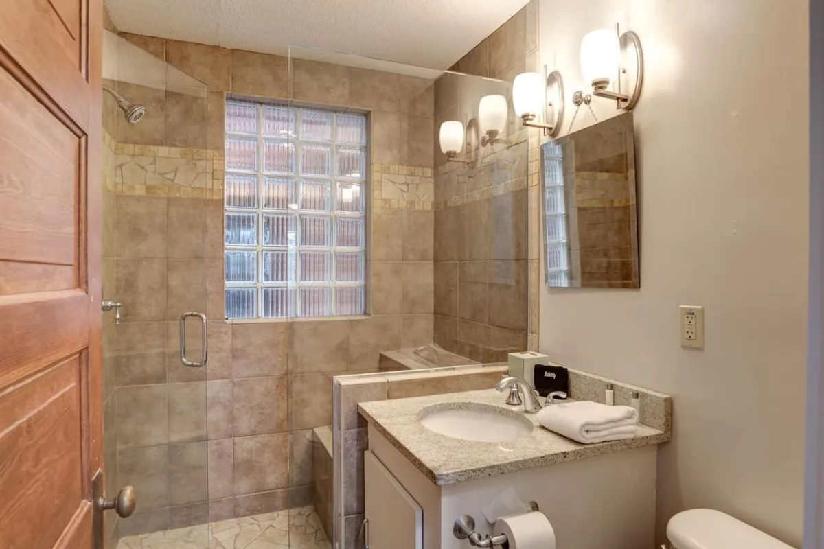 A contemporary bathroom with a glass block window that lets in soft natural light, a modern vanity with sink, and stylish light fixtures. The space feels fresh and inviting, ideal for unwinding after a busy day.