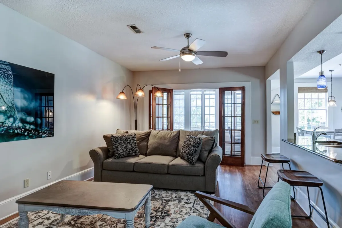 A stylish living room with a cozy sofa, contemporary art on the wall, and large windows flooding the space with natural light. The scene conveys relaxation and sociability, with inviting seating and thoughtful decor.