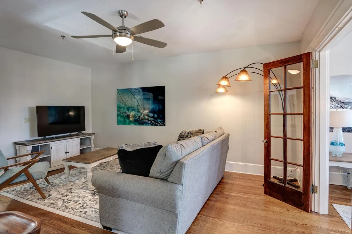 A cozy and inviting living room space featuring a comfortable sofa, a TV, stylish artwork above the seating area, and a floor lamp, all set in a well-lit atmosphere. The room feels welcoming and is designed for relaxing or socializing after a day exploring Asheville.