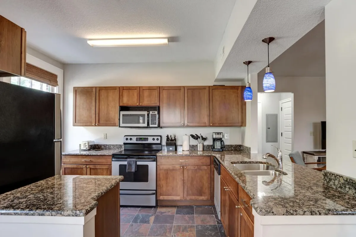 A modern kitchen with granite countertops, wood cabinetry, stainless steel appliances, and pendant lighting. The space feels inviting and functional, ready for everything from quick breakfasts to lively dinner gatherings.